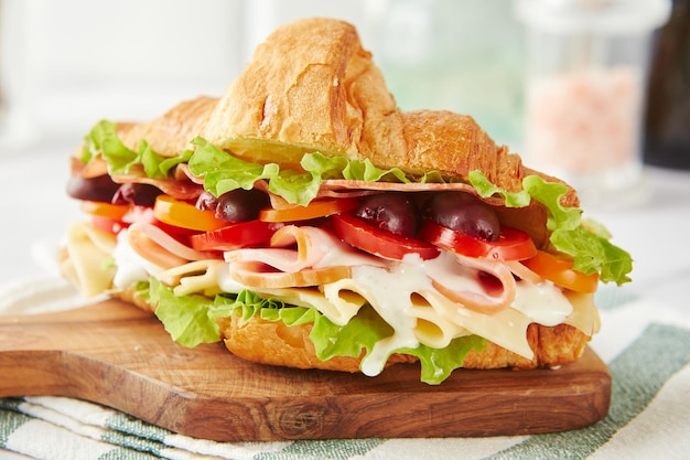 Croissant-Sandwich mit Käse-Schinken-Salat-Tomaten-Oliven und köstlicher Soße auf Holzbrett