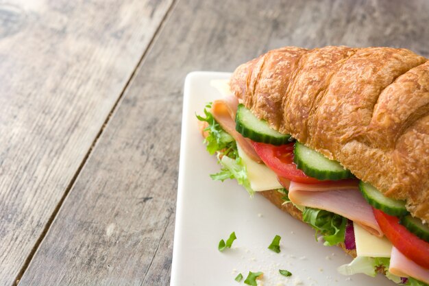 Croissant-Sandwich mit Käse, Schinken und Gemüse auf Holztisch, Kopierraum