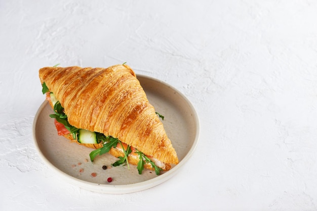 Croissant-Sandwich mit Lachs-Fisch-Frischkäse-Gurke und Rucola auf einem Teller