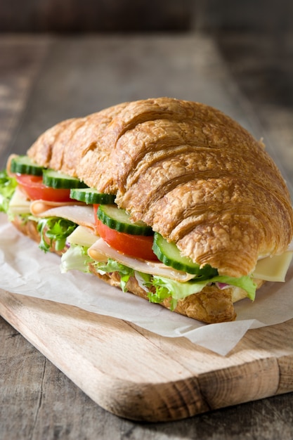 Croissant sandwich con queso, jamón y verduras en la mesa de madera