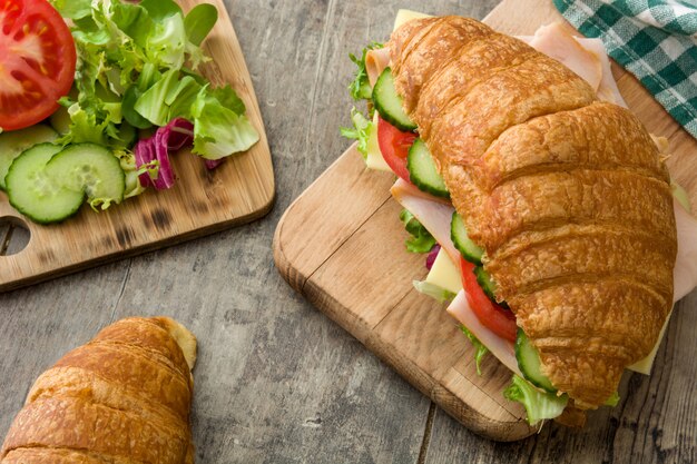 Croissant sandwich con queso, jamón y verduras en la mesa de madera