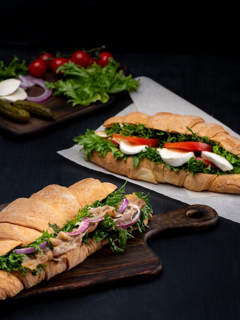 Croissant-Sandwiches mit frischem Gemüse und Schinken auf schwarzem Holzhintergrund