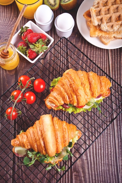 Croissant-Sandwiches mit Schinken, Käsegrün mit Waffeln, Honig, Erdbeeren und Tomaten