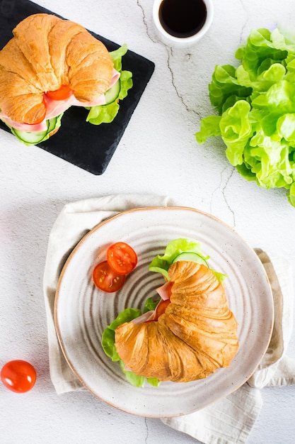 Croissant-Sandwiches mit Schinkensalat und Gemüse auf einer Schiefertafel auf der Tischplatte und vertikale Ansicht