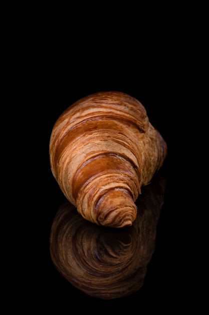 Croissant sobre fondo negro de estudio reflectante. Fondo reflejado espejo brillante negro aislado para cada concepto.