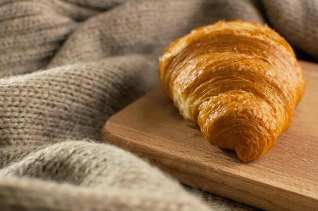 Croissant sobre una tabla de madera en el fondo de un plaid tejido