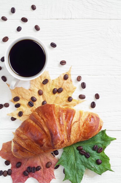 Croissant, Tasse Kaffee und Herbstlaub auf dem Tisch, Draufsicht