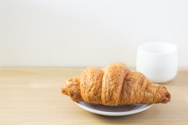 croissant y taza de café con leche en la placa de madera