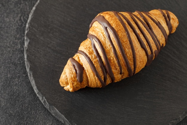 Croissant vertido con chocolate en una placa de piedra de pizarra con fondo oscuro y enfoque selectivo