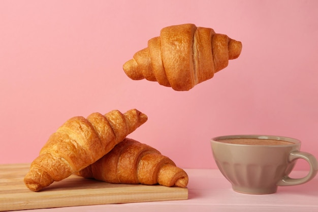 Croissant volador con café sobre fondo rosa