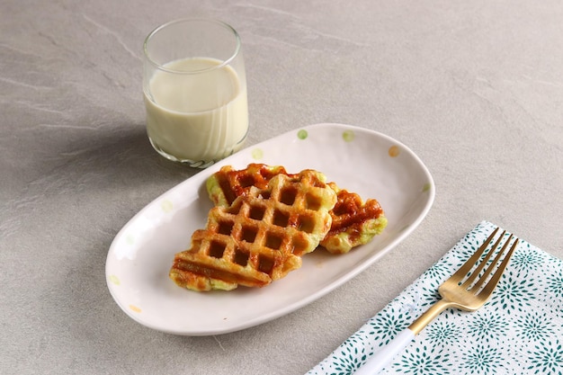 Foto croissant waffle o croffle con un vaso de leche matcha servido en el plato ovalado con tenedor.