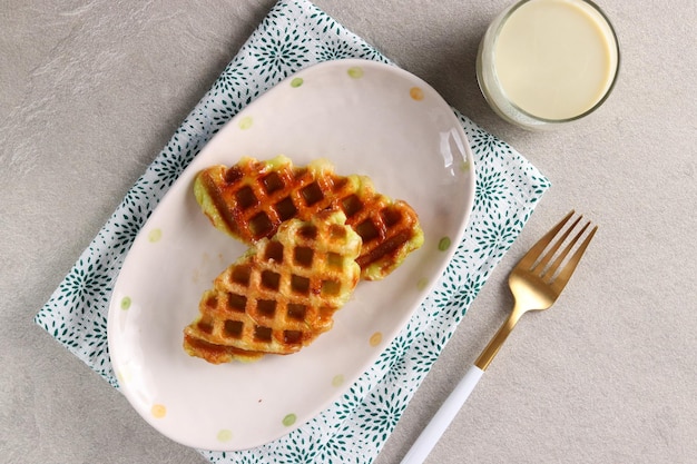 Croissant Waffle o Croffle con un vaso de leche matcha servido en el plato ovalado con tenedor.