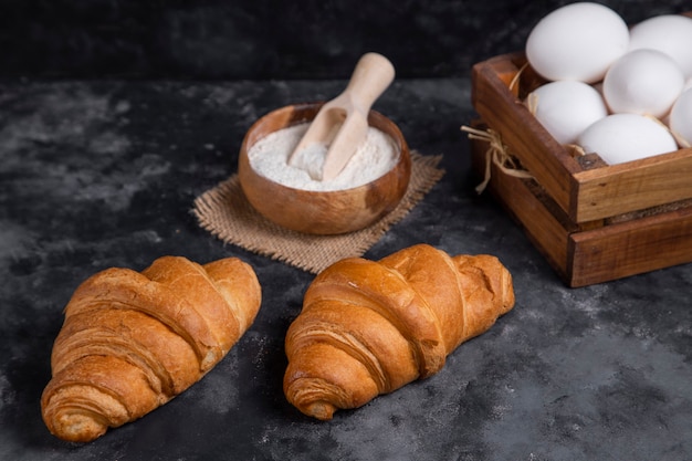 Croissants acabados de fazer com ovos de galinha e tigela de madeira com farinha.