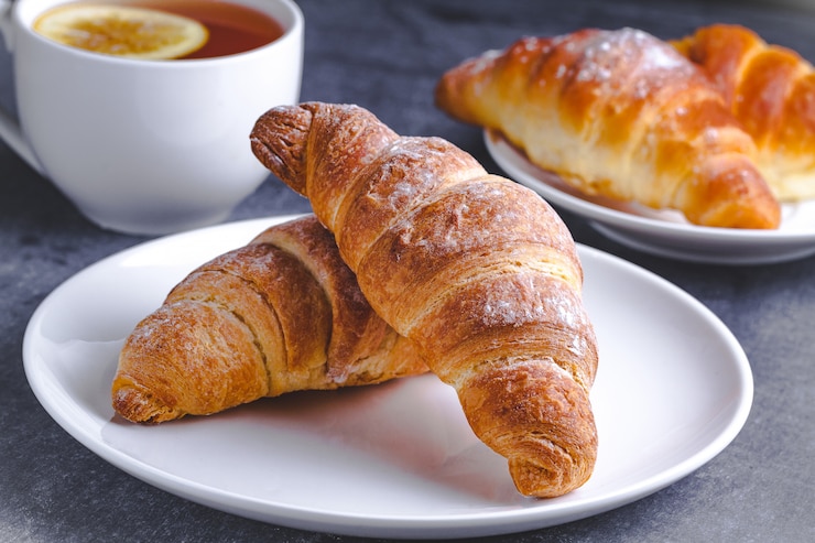 Foto croissants acabados de fazer e uma xícara de chá quente com limão no café da manhã tradicional francês em um fundo escuro