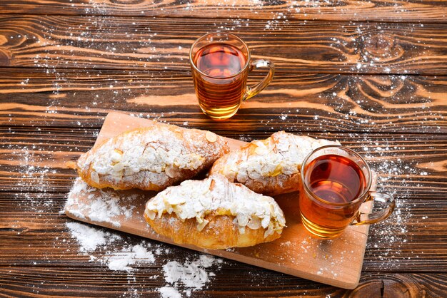 Croissants con almendras y té en una mesa de madera.