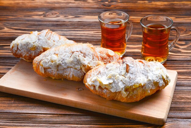 Croissants con almendras y té en una mesa de madera.