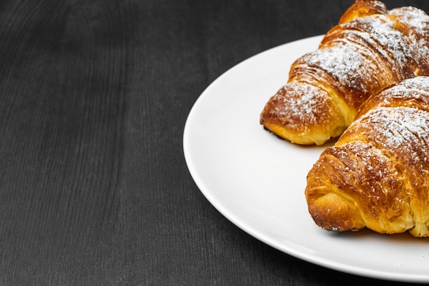 Croissants amanteigados deliciosos em uma placa branca em um fundo preto de madeira com espaço da cópia.