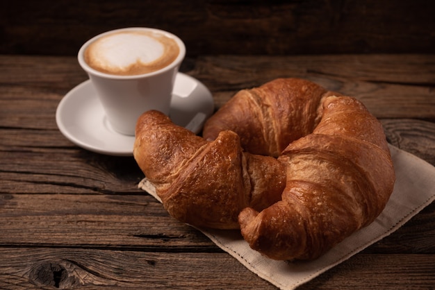 Croissants amanteigados frescos com café em uma mesa de madeira rústica close-up