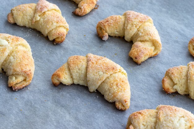 Croissants assados de massa de queijo cottage com açúcar em uma assadeira com papel manteiga