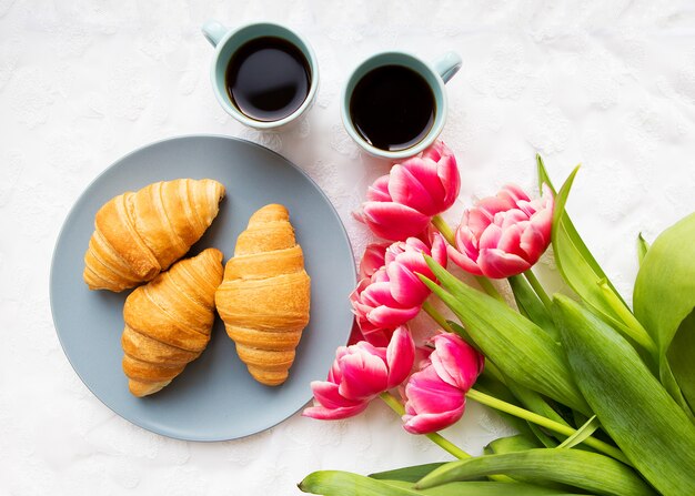 Croissants, café y un ramo de tulipanes rosados.