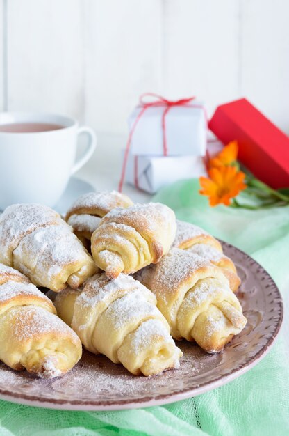 Croissants caseros con mermelada de frutas, decorados con azúcar en polvo y una taza de té de la mañana