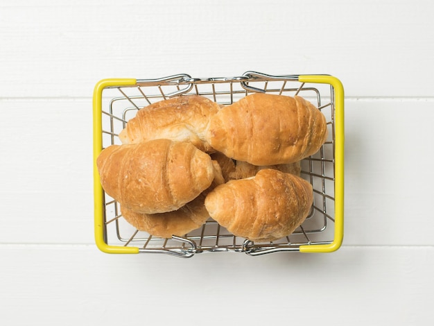 Unos croissants en una cesta de hierro sobre una mesa blanca La vista desde arriba