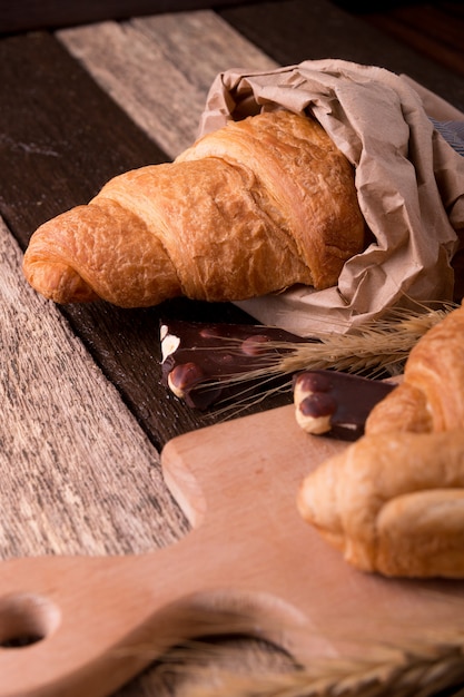 Croissants con chocolate a bordo cerca de trigo en superficie de madera de saco