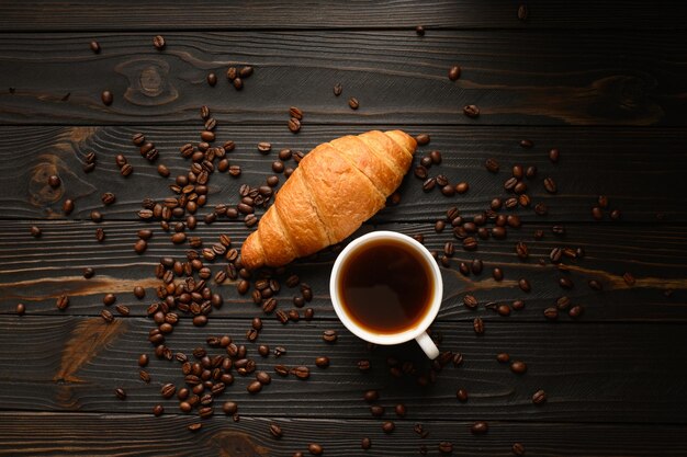 Croissants com café e grãos de café em um fundo de madeira