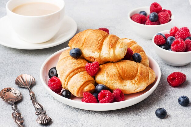 Croissants com framboesas frescas e mirtilos em fundo cinza de concreto. copie o espaço. conceito de café da manhã café mel