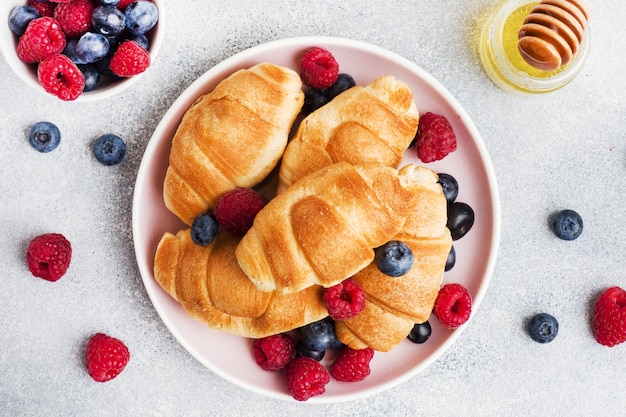 Croissants com framboesas frescas e mirtilos na mesa de concreta cinza. copie o espaço. conceito de café da manhã café mel