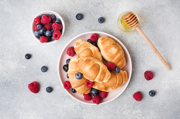 Croissants com framboesas frescas e mirtilos na superfície de concreto cinza