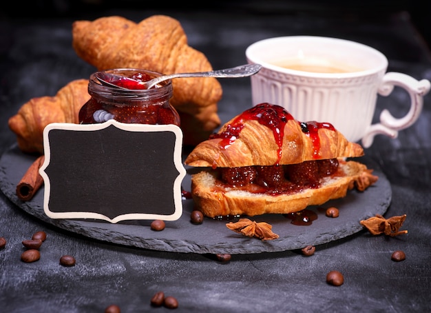 Croissants com geléia de framboesa e placa de madeira preta vazia