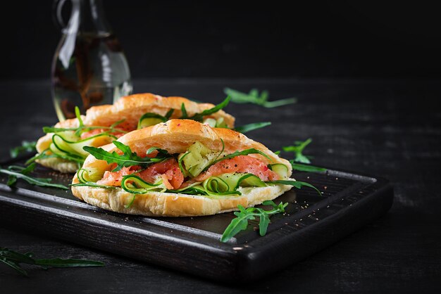 Croissants com pepino de salmão salgado e rúcula servido em fundo escuro Fechar