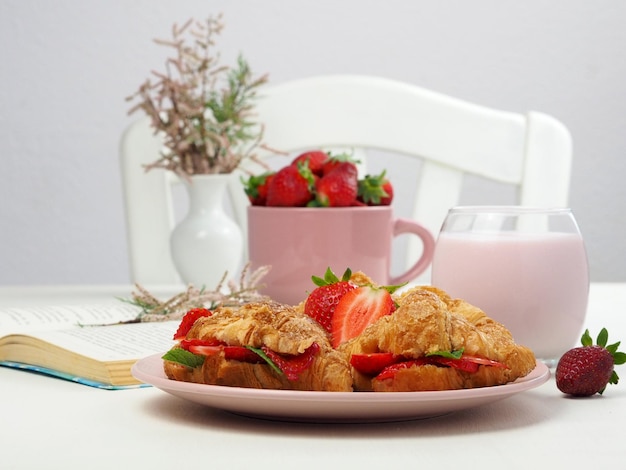 Croissants com recheio de morango morangos frescos um livro e um vaso de flores sobre uma mesa branca
