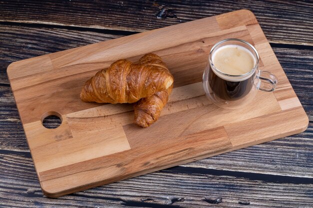 Croissants com uma xícara de café em uma placa de madeira.