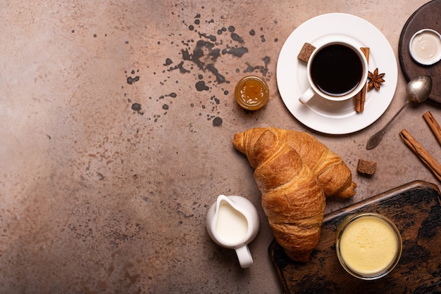 Croissants crujientes con café negro y jugo de naranja en una mesa de madera, vista superior