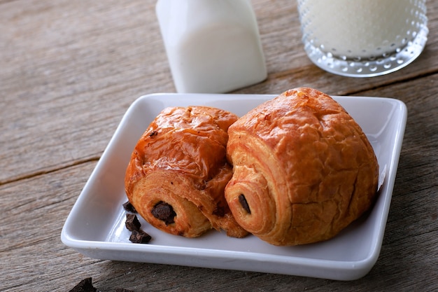 Croissants de Chocolate Fresco Assado (Pain au Chocolat) com Leite no Café da Manhã. Servido em prato branco em mesa rústica Copiar espaço para texto