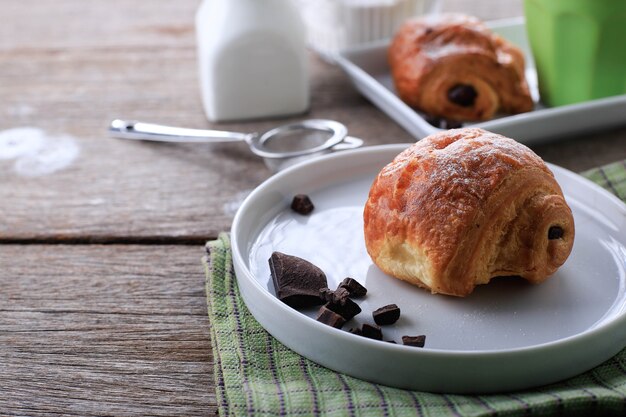 Croissants de Chocolate Fresco Assado (Pain au Chocolat) com Leite no Café da Manhã. Servido em prato branco em mesa rústica Copiar espaço para texto