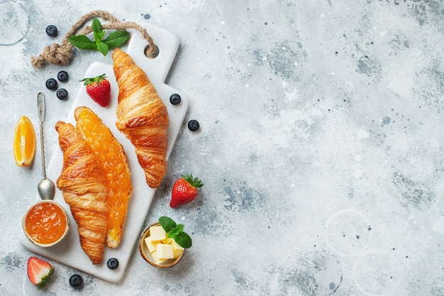 Croissants doces frescos com manteiga e geleia de laranja no café da manhã. café da manhã continental em uma mesa de concreto branca. vista do topo. postura plana.