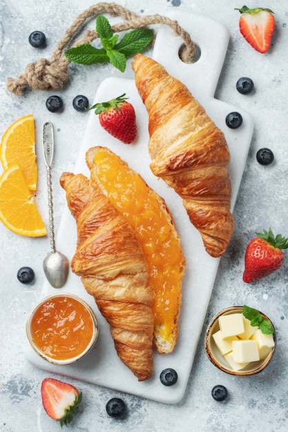 Croissants dulces recién hechos con mantequilla y mermelada de naranja para el desayuno.