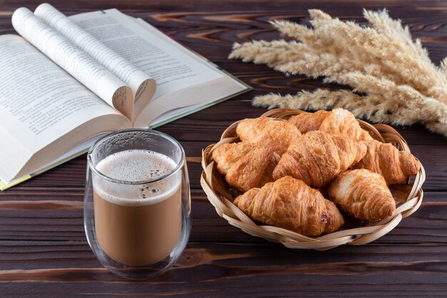 Croissants e um copo de café com leite na mesa de madeira marrom escura