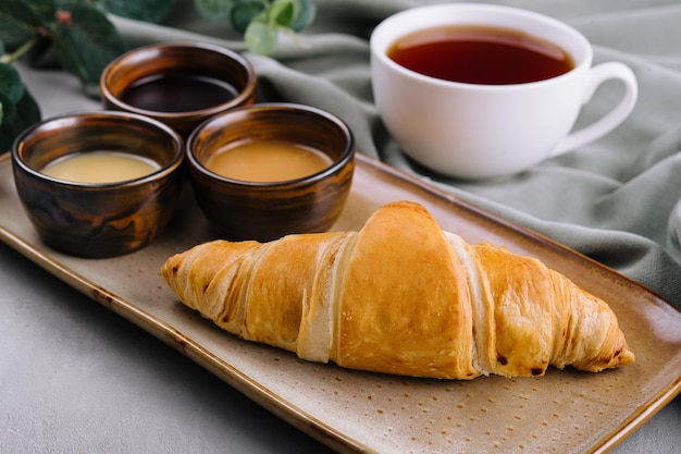 Croissants franceses frescos con chocolate en un plato, mermelada de arándanos, miel y té.