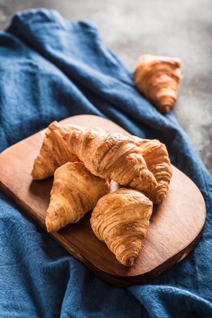 Croissants franceses recién horneados en una tabla de madera sobre una mesa de luz con una servilleta azul.