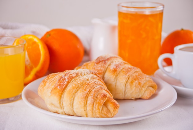 Croissants frescos, pães, laranjas, geléia de laranja e suco. Conceito de pequeno-almoço.