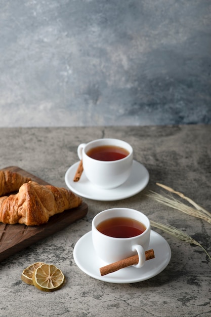 Croissants frescos y sabrosos con dos tazas de té caliente colocados sobre la mesa de piedra