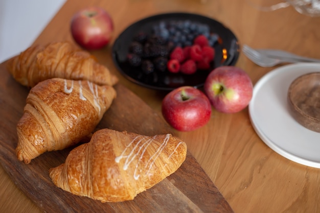 Croissants grandes, frutas vermelhas, maçãs em uma mesa de madeira