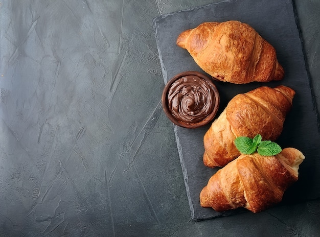 Foto croissants horneados con chocolate para untar en mesa negra. vista superior del desayuno