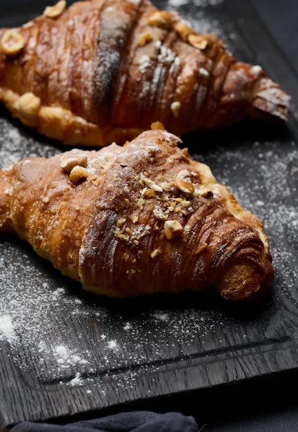 Croissants horneados sobre una tabla de madera negra espolvoreados con azúcar en polvo