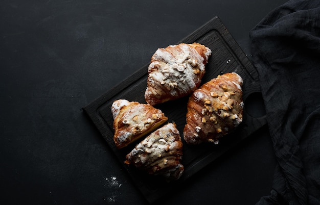 Croissants horneados en una tabla de madera negra espolvoreada con vista superior de azúcar en polvo