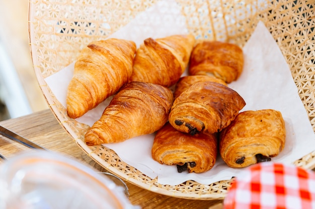 Croissants de mantequilla clásicos recién horneados y croissant de pasas dentro de la cesta de tejido.